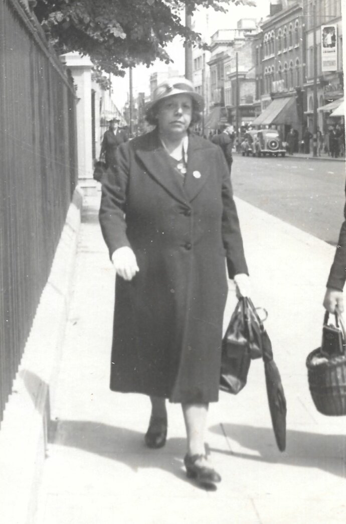 Woman wearing a long coat and hat walking down a sidewalk.