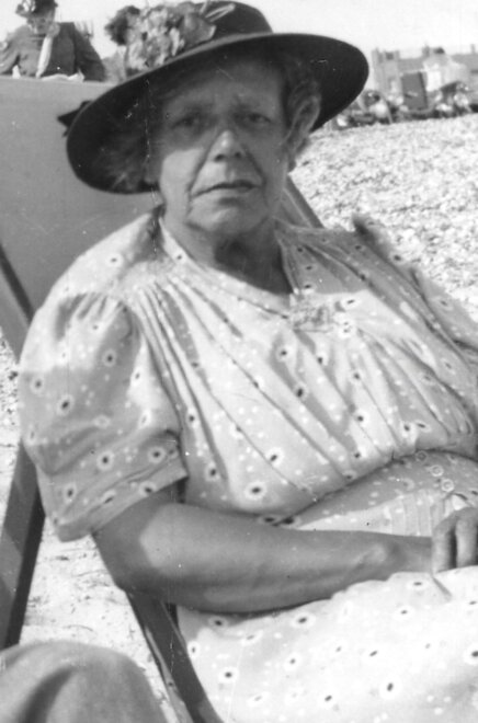 Woman in a sunhat and dress sitting in a chair on the beach.