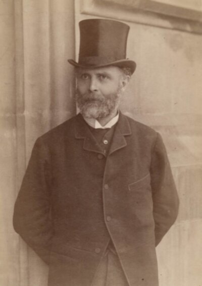 Man in a top hat and coat leaning against a wall.