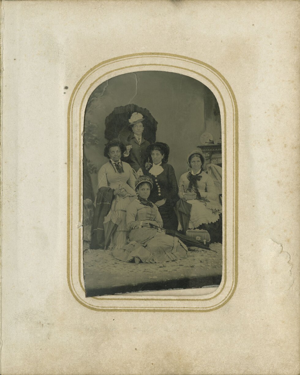 Group of women in dresses, some seated and some standing.