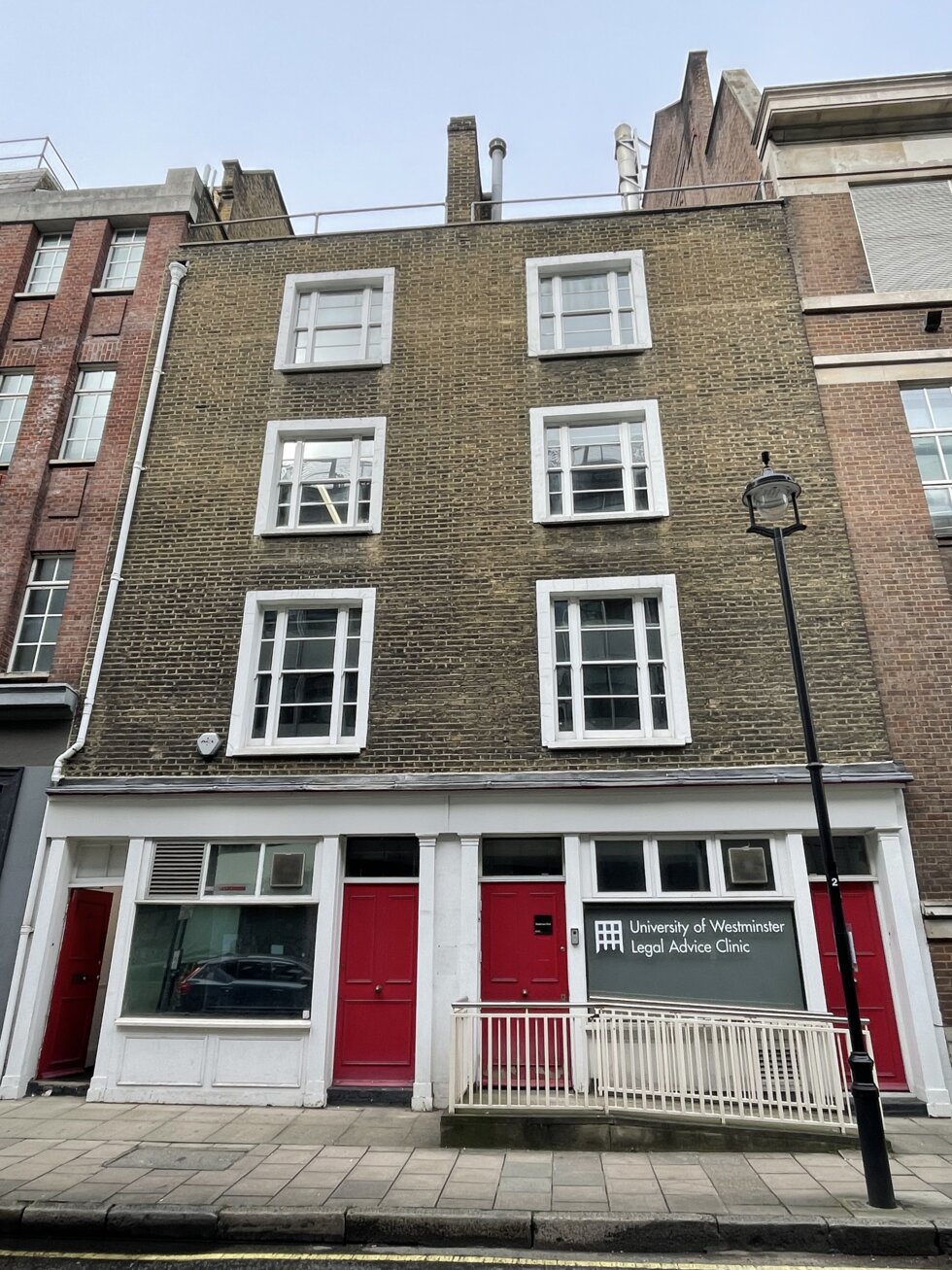 Front of a four-story brick building with red doors and street lamp in front.