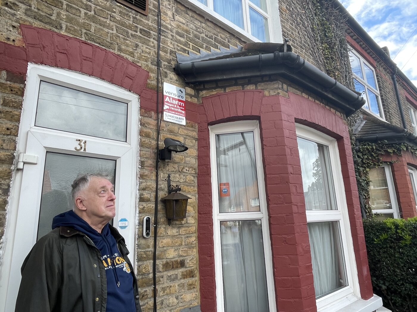 Man stands in front of door of brick house with red trim.