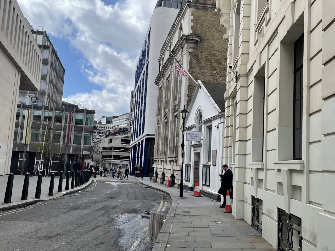 Empty city street with large buildings on both sides and sidewalk on one side.