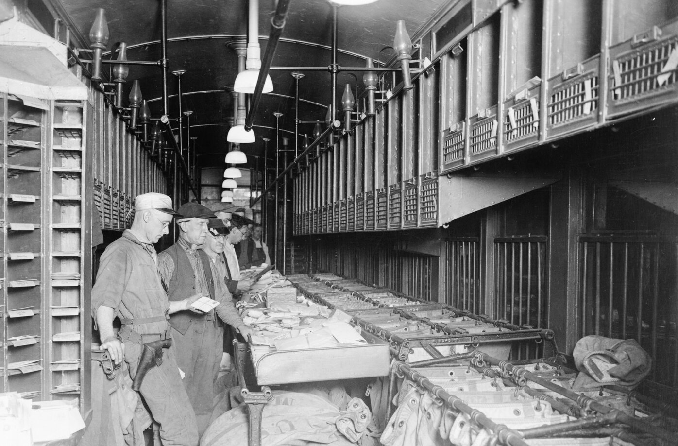 Group of men standing in a single line sorting mail inside a train car.