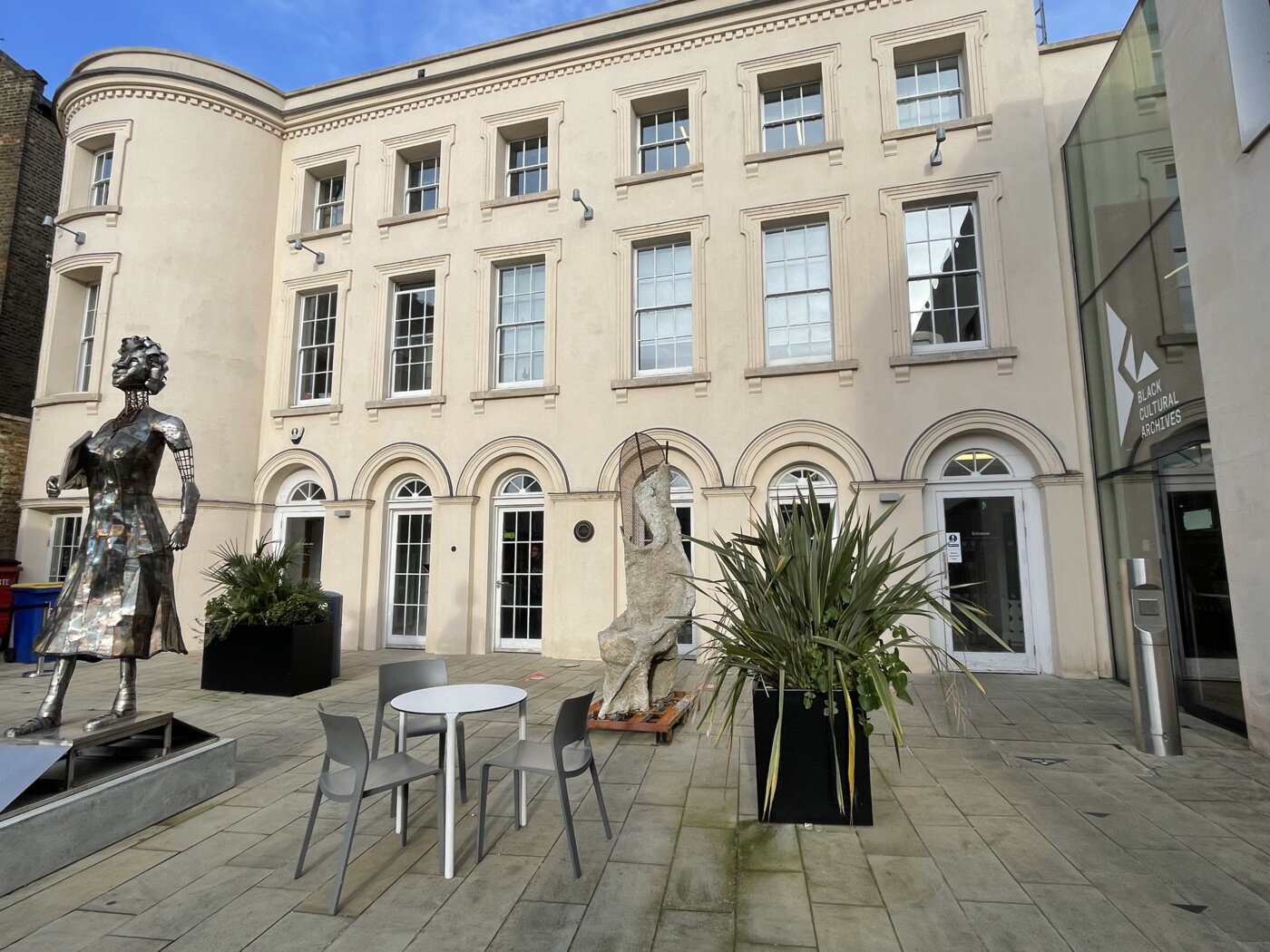 Exterior of three-story cream colored building with lots of windows and a sculpture in front.