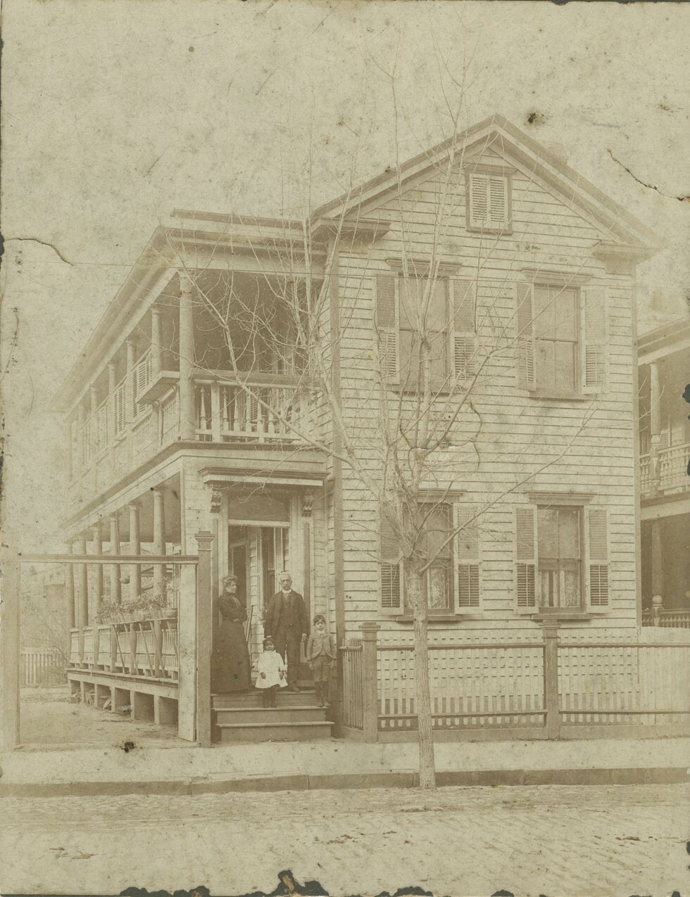 Two adults and two children stand on the steps of a two-story house.
