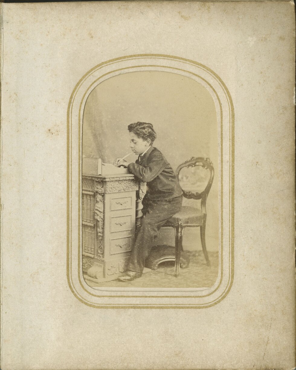 A boy sits writing at a wooden desk.