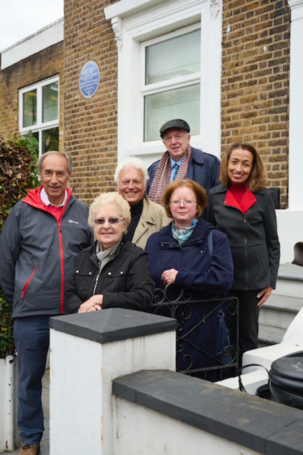 A small group of people stand on the stairs in front of a house.