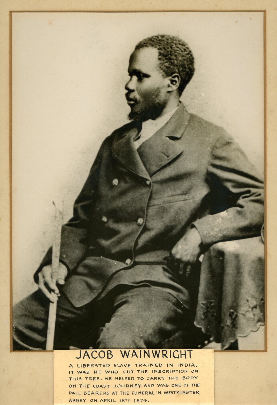 Seated, half-body portrait of Abdullah Susi in half profile, holding walking stick.