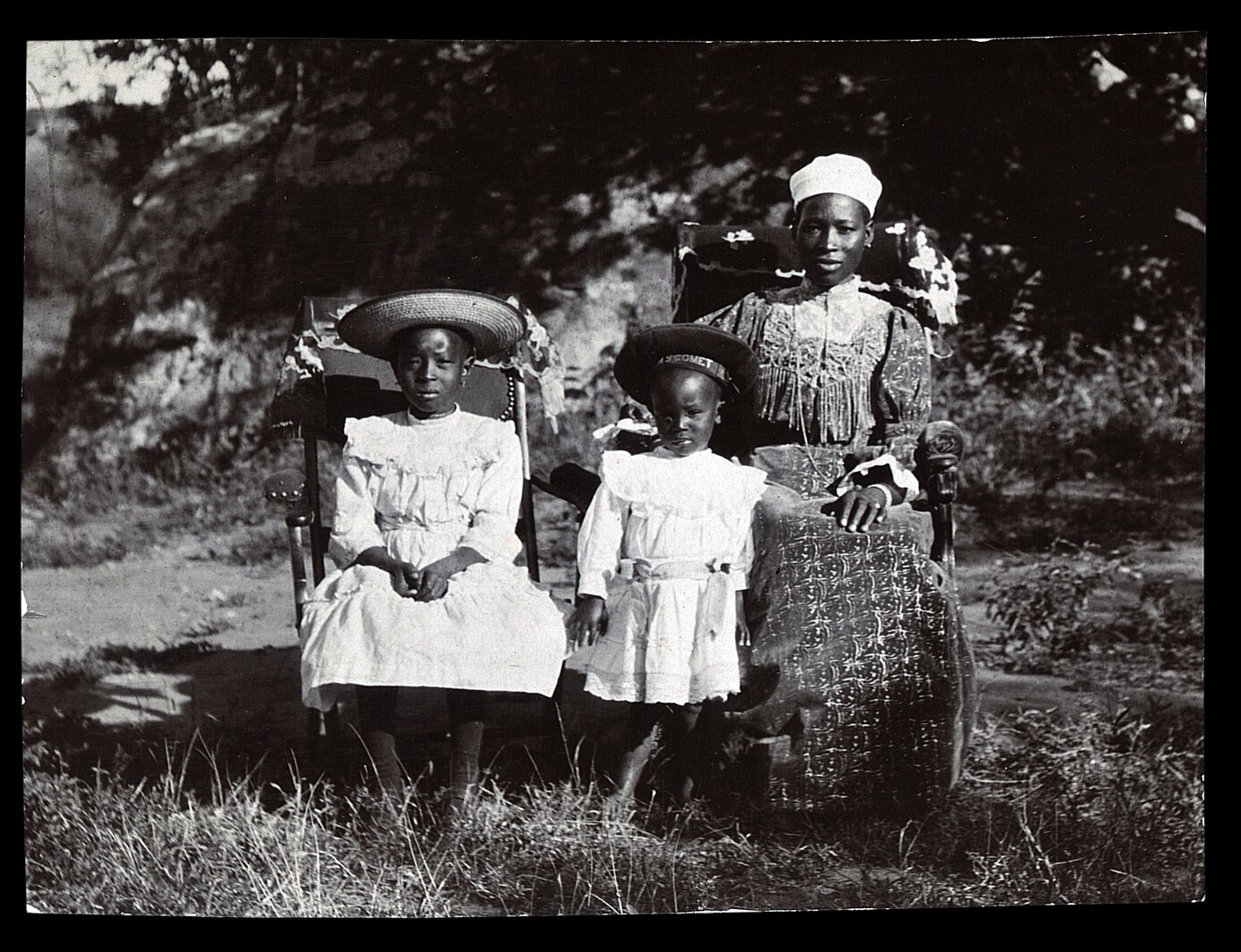 Semane Khama at right, seated, with two children, one of whom is standing, one of whom is seated.