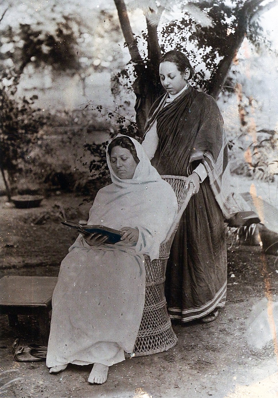 Pandita Ramabai Sarasvati seated, reading a book, with Monramabai looking over Sarasvati's shoulder.