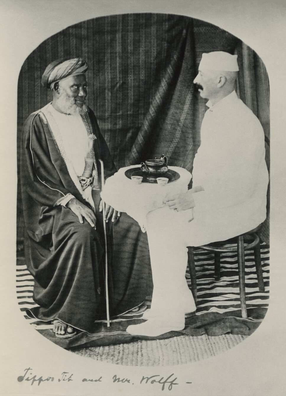 Tippu Tip and Eugene Wolf seated and facing one another in half profile.
