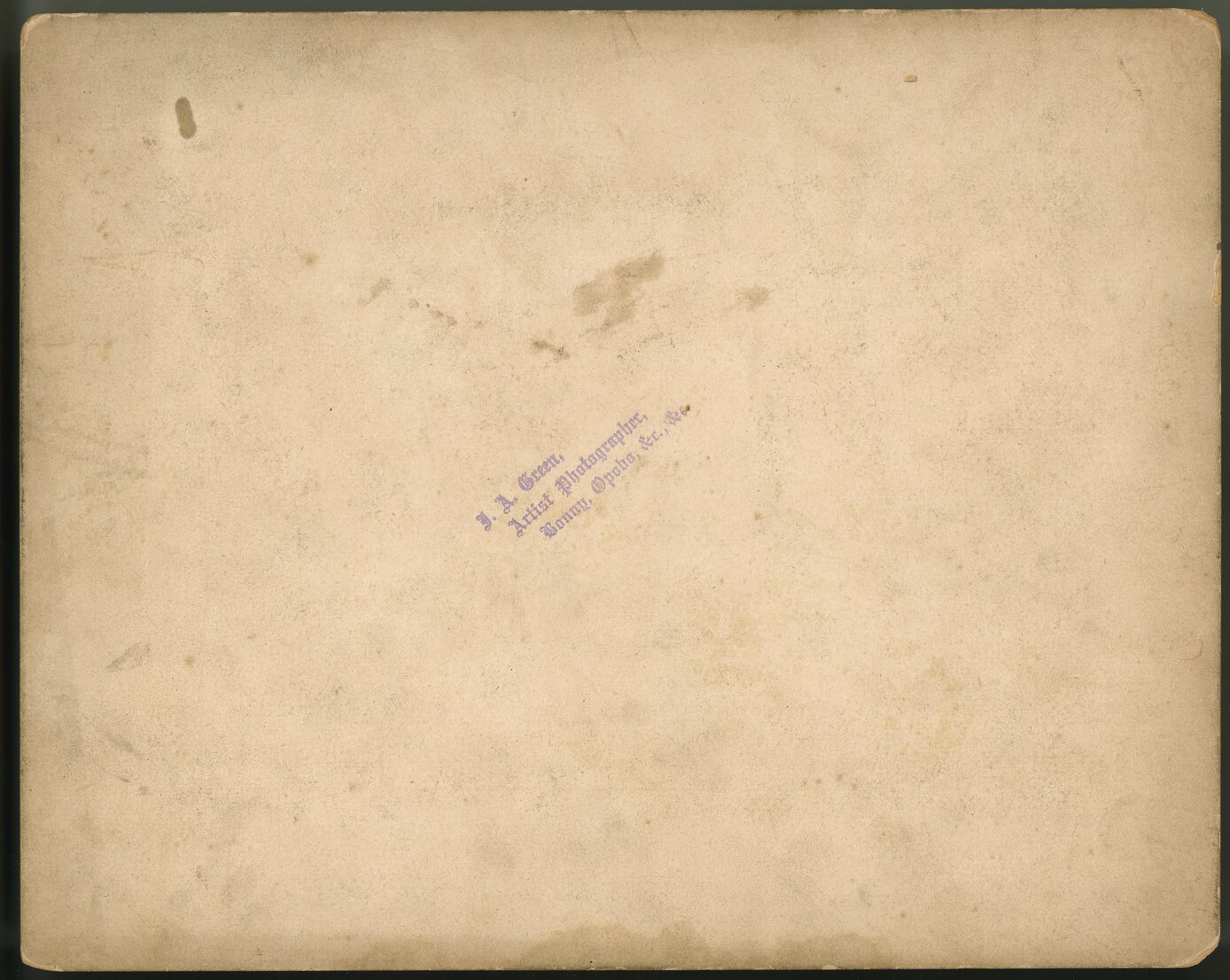 Stained paper with a diagonol purple stamp that says, “J.A. Green, Artist Photographer, Bonny Opobo, &c, &c