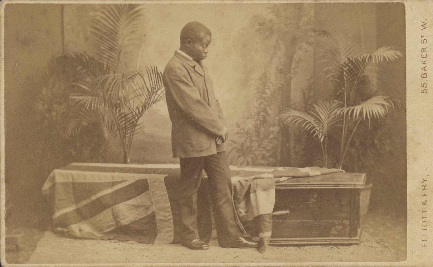 Jacob Wainwright standing with head bowed before a coffin which is partly covered by a British flag.