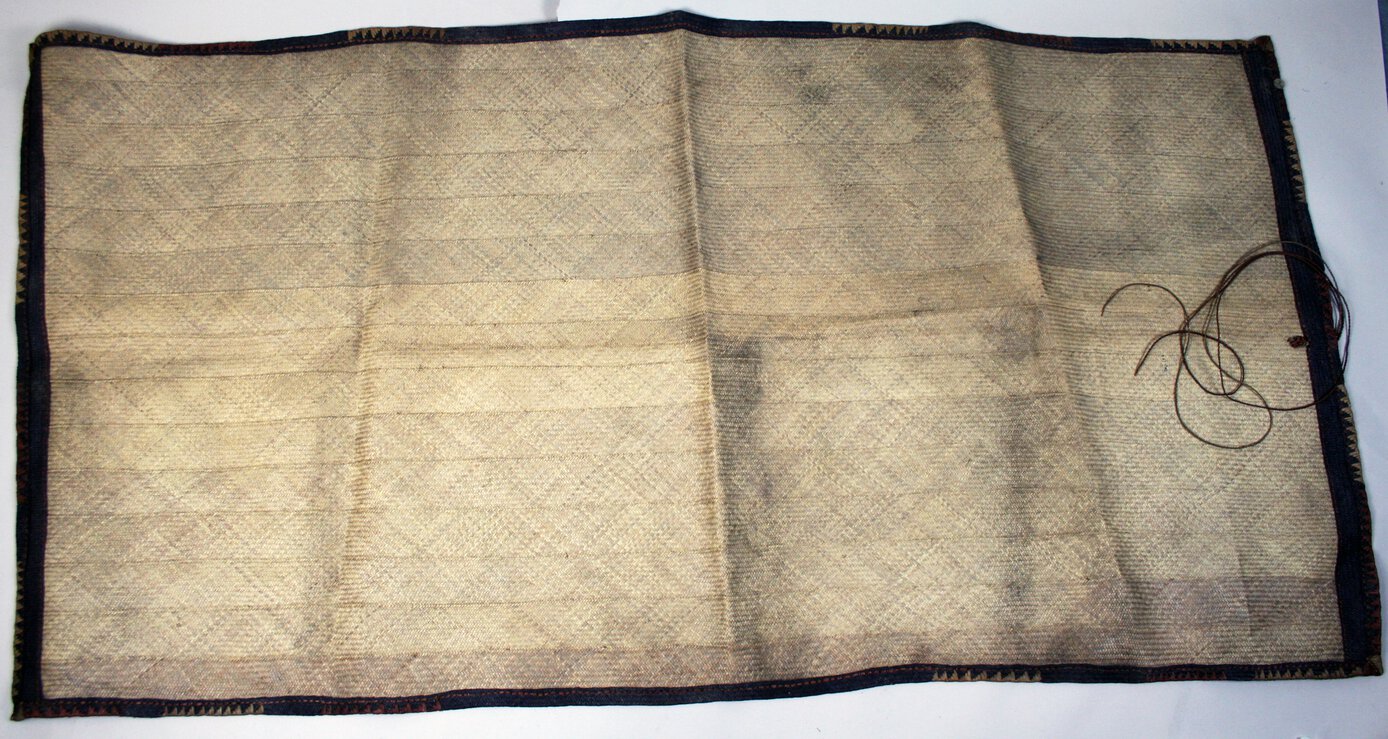 Large plaited palm leaf travelling mat, plain and undyed except for black, red-ochre, and plain decorative boarder strip running round the edges of the mat.