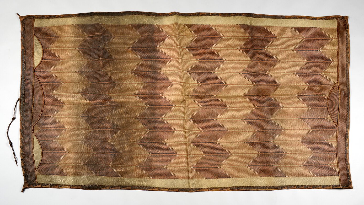 Large plaited palm leaf mat, decorated with six broad, zig-zag bands running horizontally.