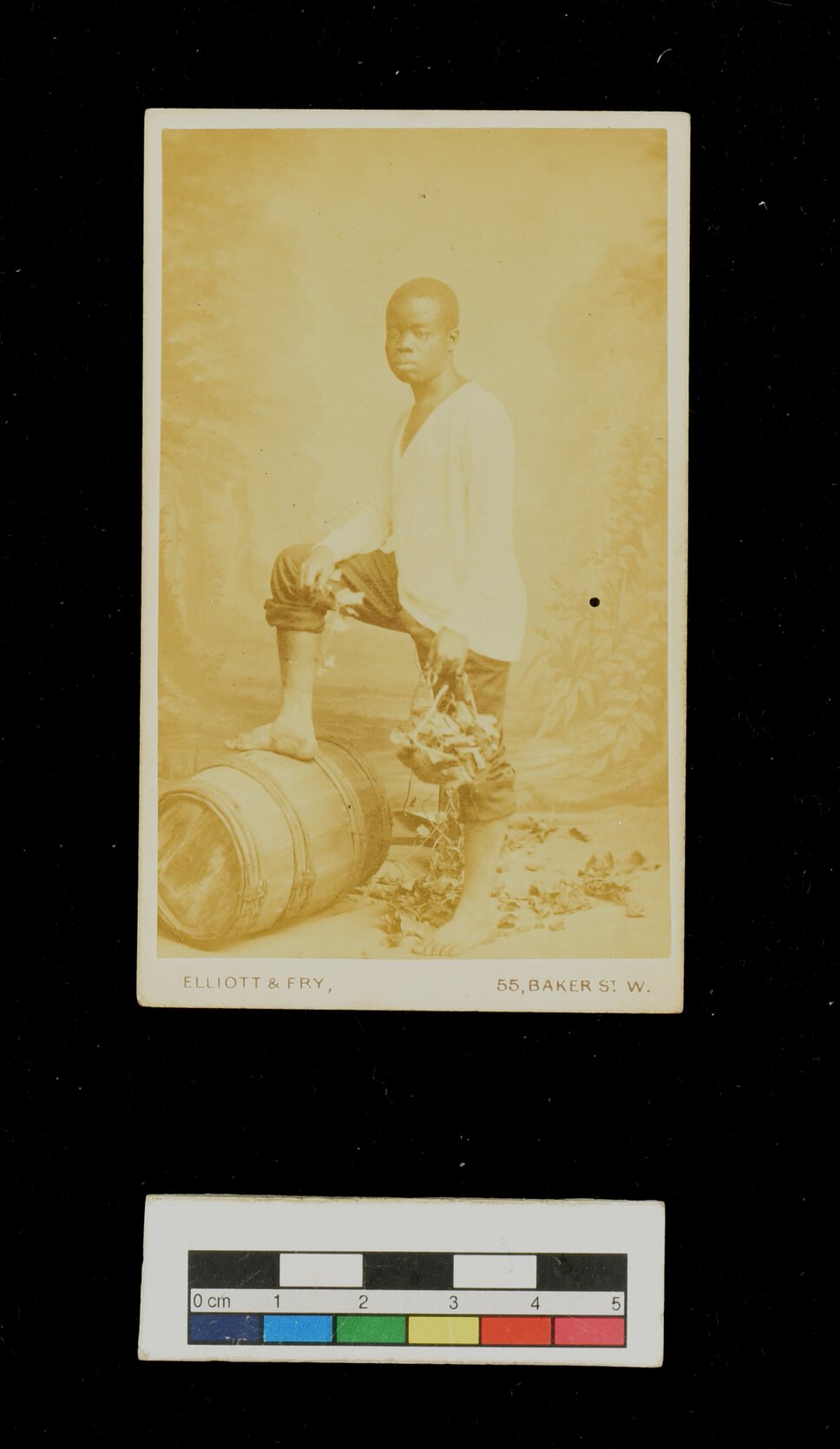 Jacob Wainwright, standing in quarter profile with one foot on barrel, holding basket with one hand. 