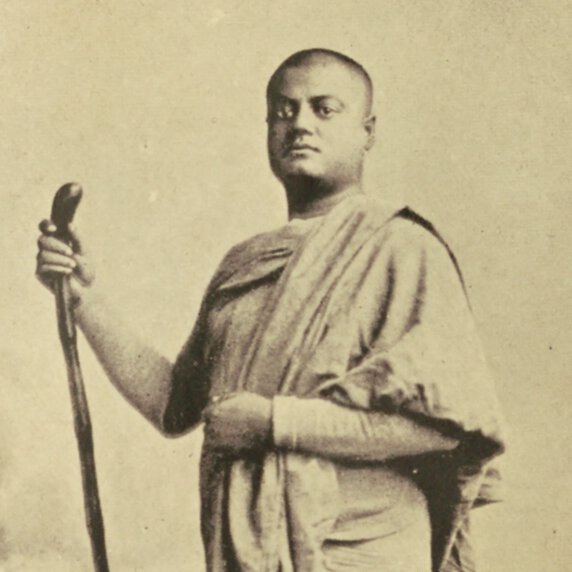 Portrait of Swami Vivekanada, standing, his body turned to the right, holding a walking stick.