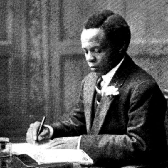 Portrait of Solomon T. Plaatje, seated, in three-quarters profile, writing at a table.