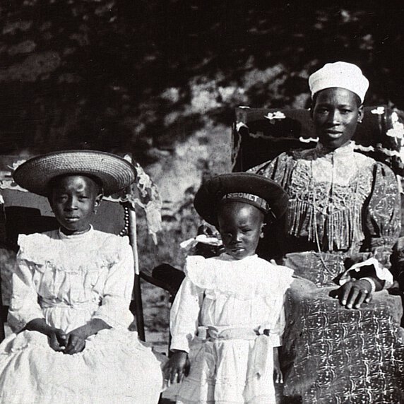 Semane Khama at right, seated, with two children at left, one of whom is standing, the other seated.
