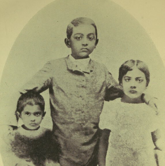 Toru, Abju, and Aru Dutt standing, facing forward, with arms around one another.