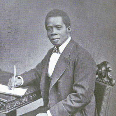 Edward Wilmot Blyden, seated at desk, writing in book, turned to his right, but facing forward.